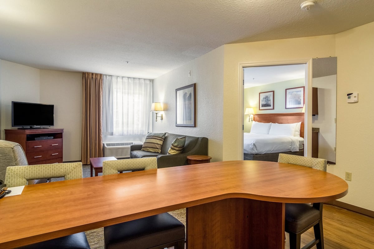 Ein Hotelzimmer mit Holztisch, einer Couch, einem Fernseher und einem Bett mit Kopfteil.
