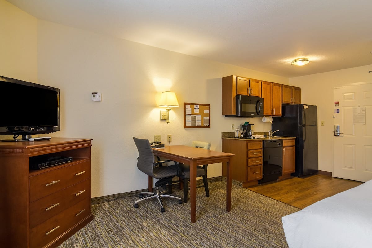 Ein Hotelzimmer mit Fernseher, Schreibtisch, Stuhl, Küchenzeile und einem Bett.
