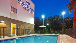 A hotel exterior with a swimming pool, outdoor seating, and a well-lit entrance. - Candlewood Suites Jacksonville East Merril Road by IHG (Jacksonville)