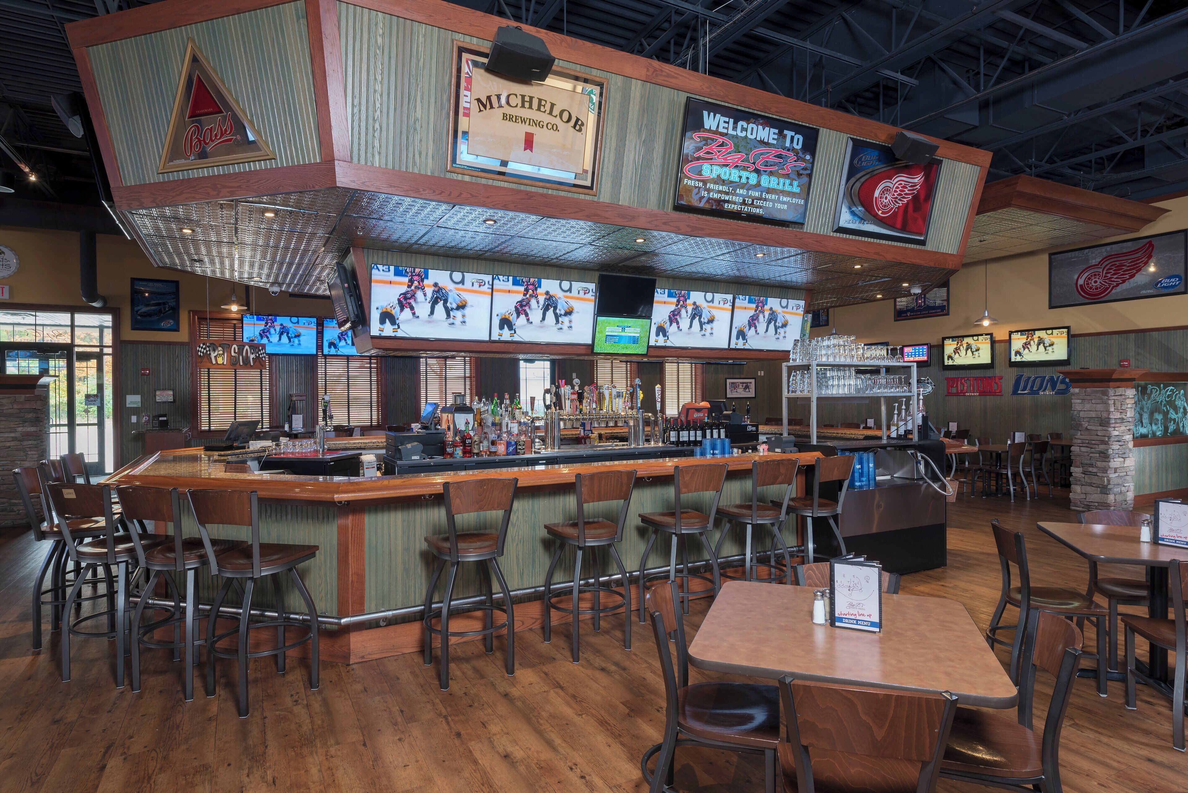 A sports bar with multiple screens displaying hockey games, a bar area with stools, and a seating section with tables and chairs.