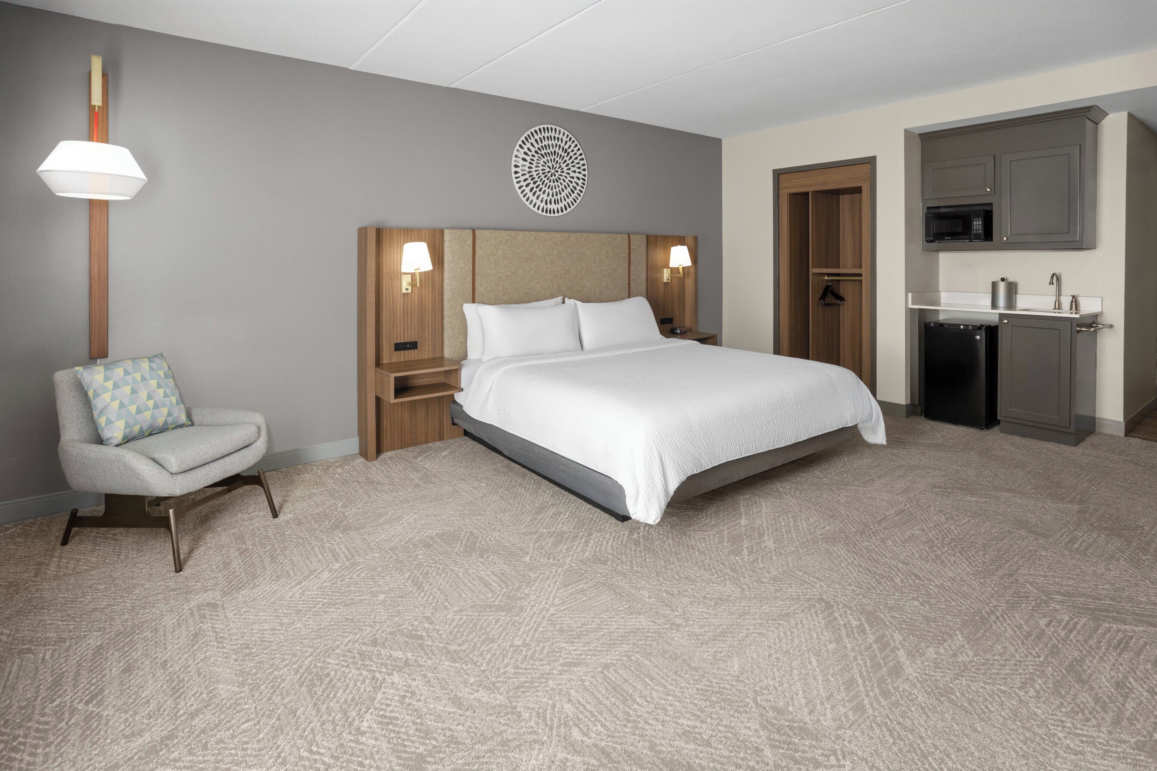 Habitación de hotel con una cama grande, una silla, un escritorio, un microondas y una pequeña cocina.