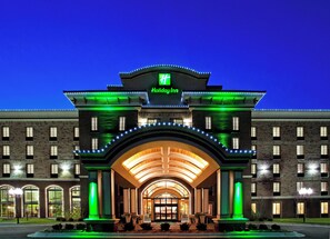 A Holiday Inn hotel with a prominent entrance, large windows, and a green-lit sign.