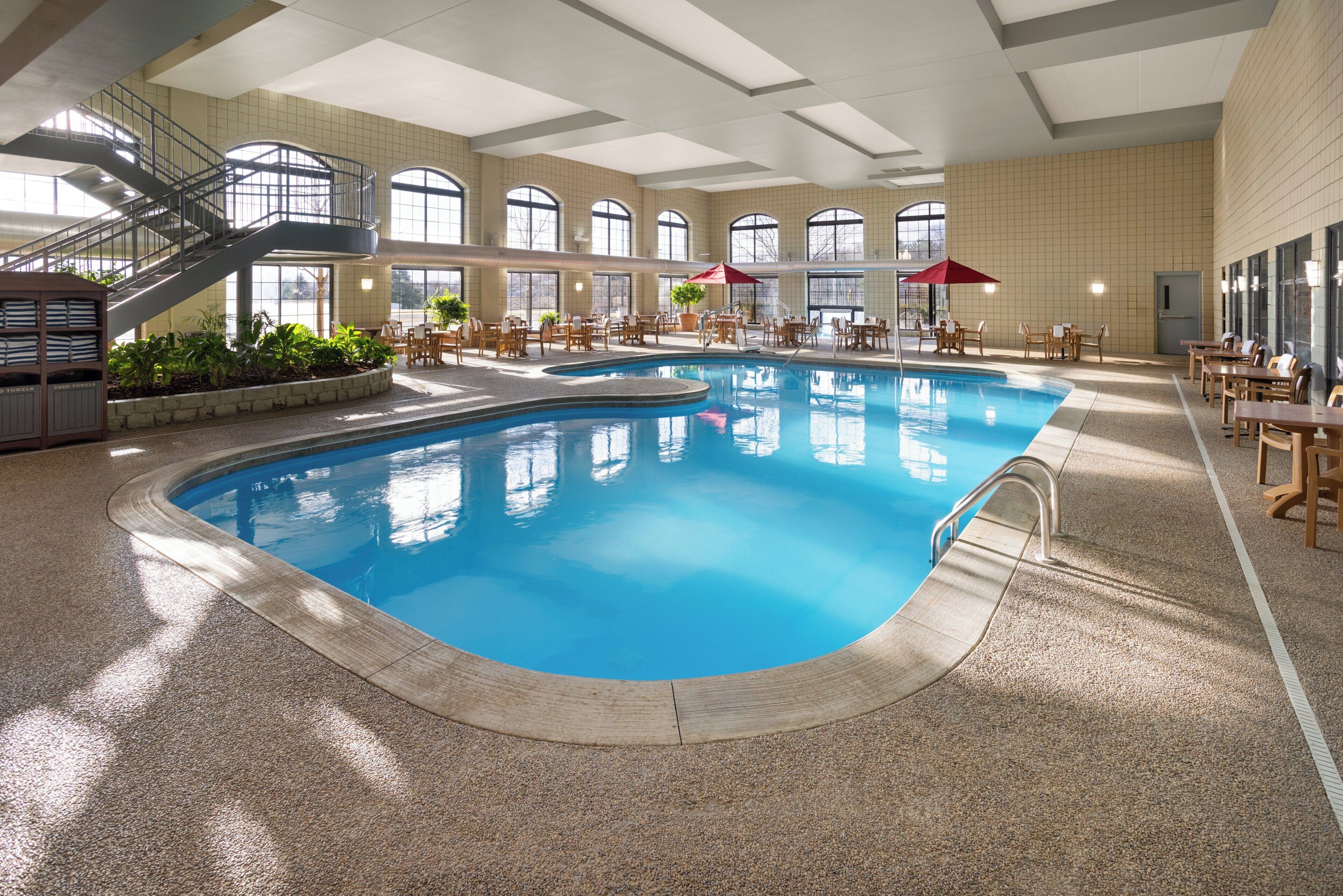 An indoor swimming pool with a clear view of the pool area, including a staircase, seating area, and potted plants.