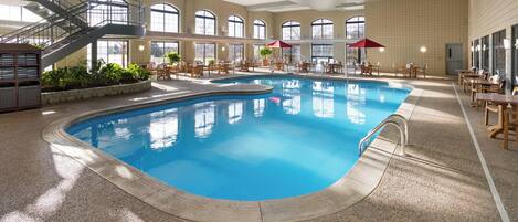 An indoor swimming pool with a clear view of the pool area, including a staircase, seating area, and potted plants.