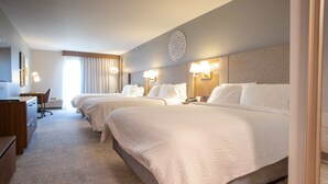 A hotel room with two beds, a desk, and a chair. There are wall-mounted lamps and a decorative wall piece.