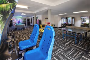 Una habitación con sillas azules, mesa de billar y juegos de arcade.