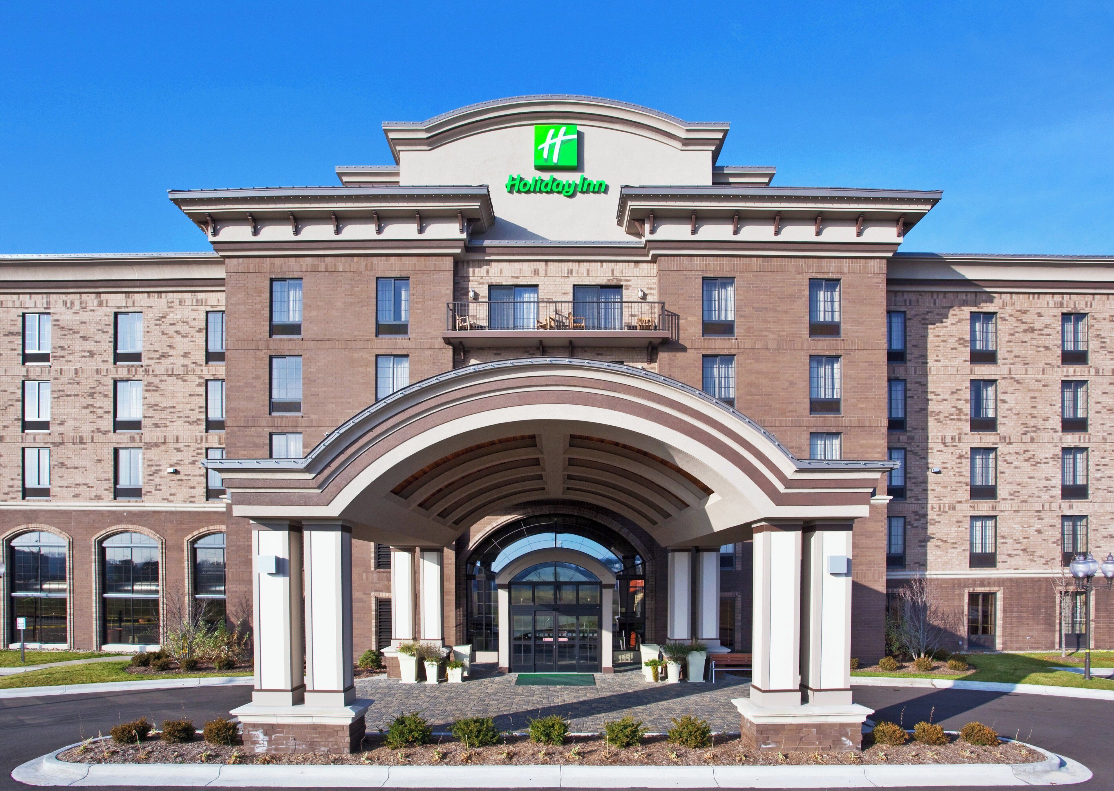 Ein Holiday Inn Hotel mit Ziegel-Fassade, großem Bogenportal und einem gut sichtbaren, grünen Logo.