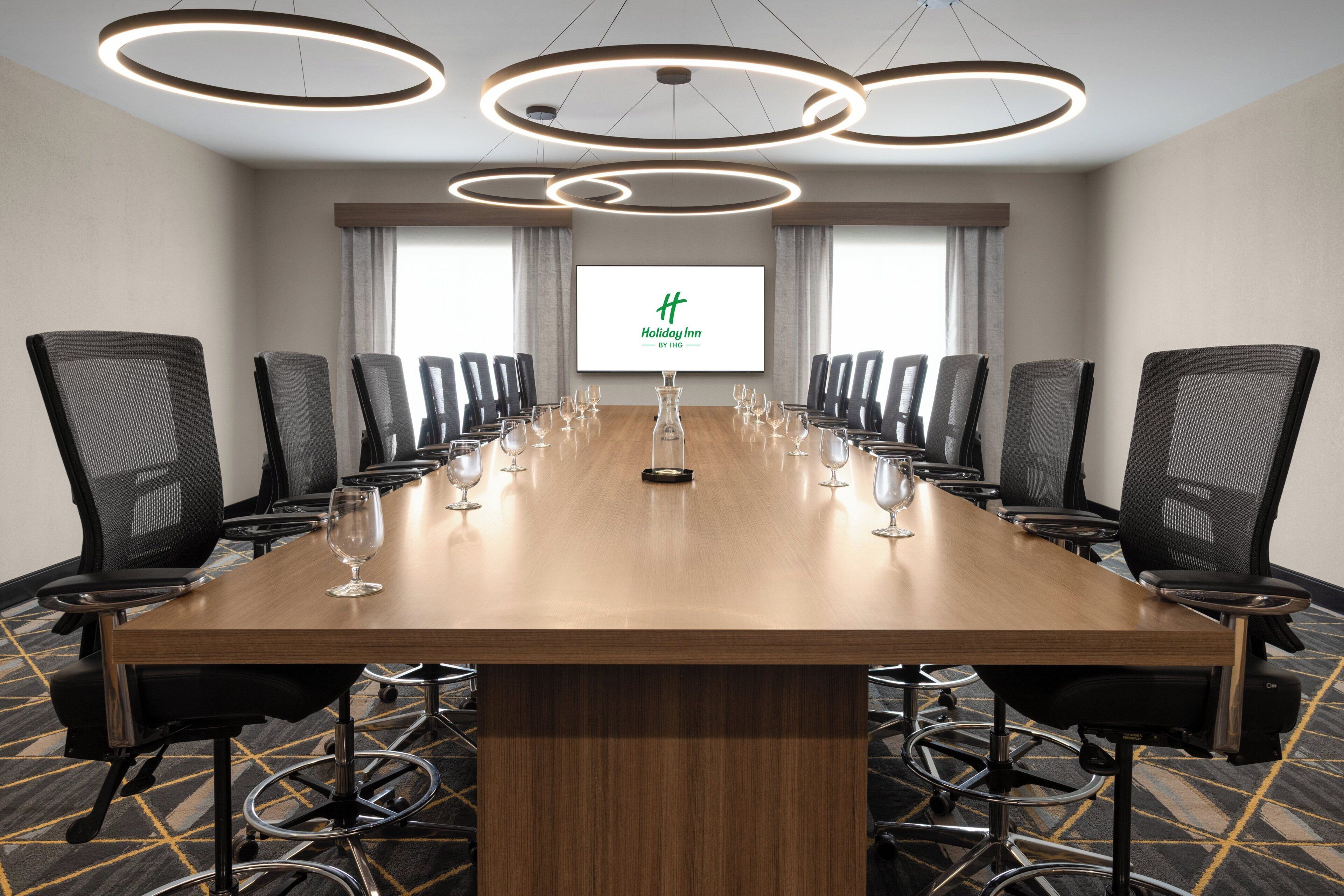 A conference room with a long table, black chairs, and a screen displaying the Holiday Inn logo.