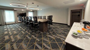 A conference room with a large table, chairs, and a buffet table with fruit.
