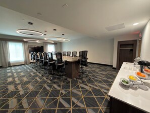 A conference room with a large table, chairs, and a buffet table with fruit.