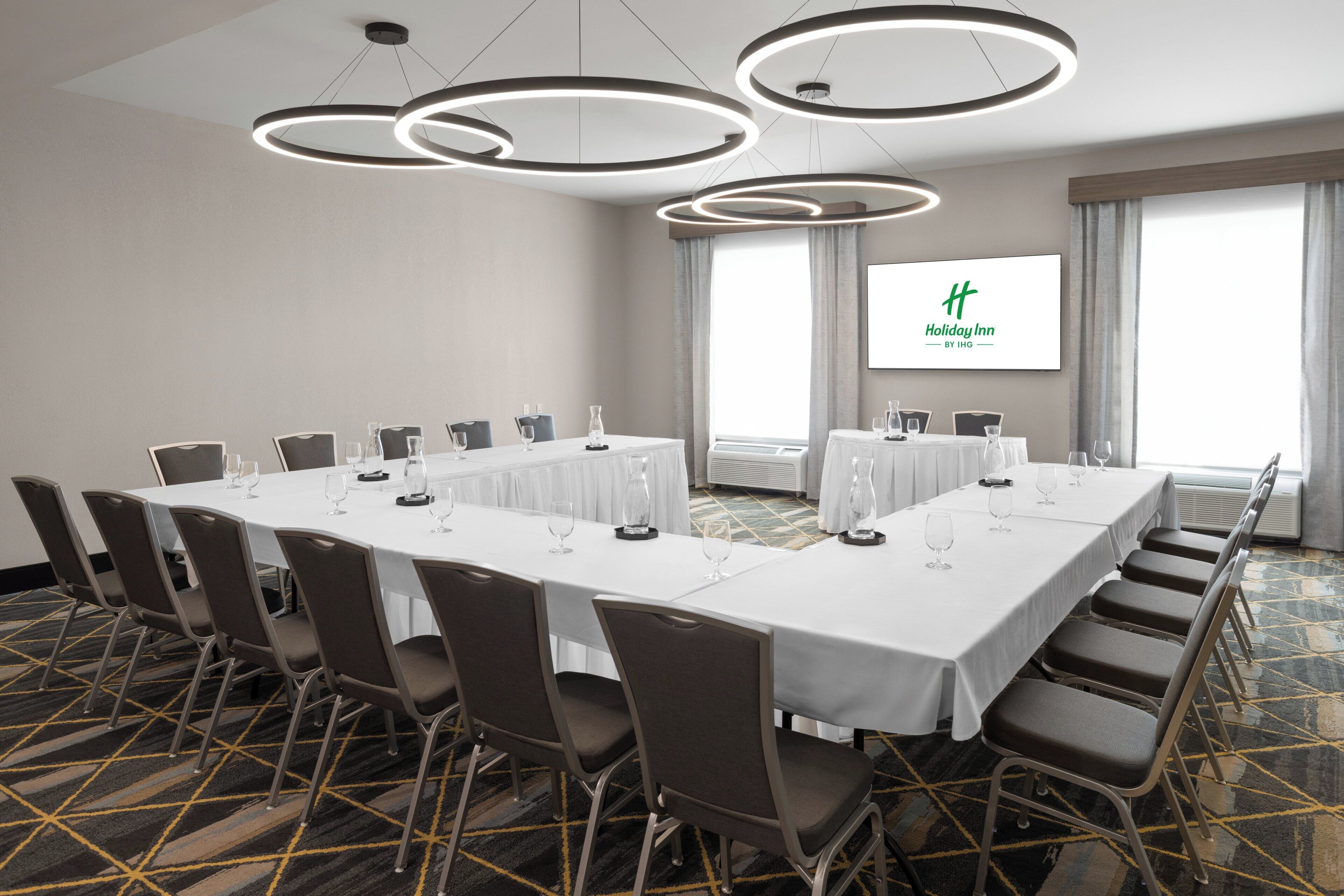 A conference room with a long table, chairs, and a screen displaying the Holiday Inn logo.