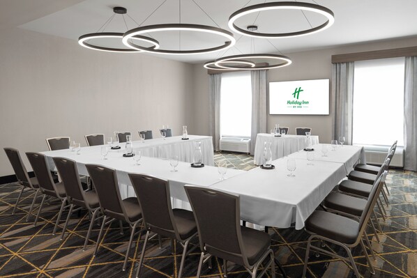 A conference room with a long table, chairs, and a screen displaying the Holiday Inn logo.