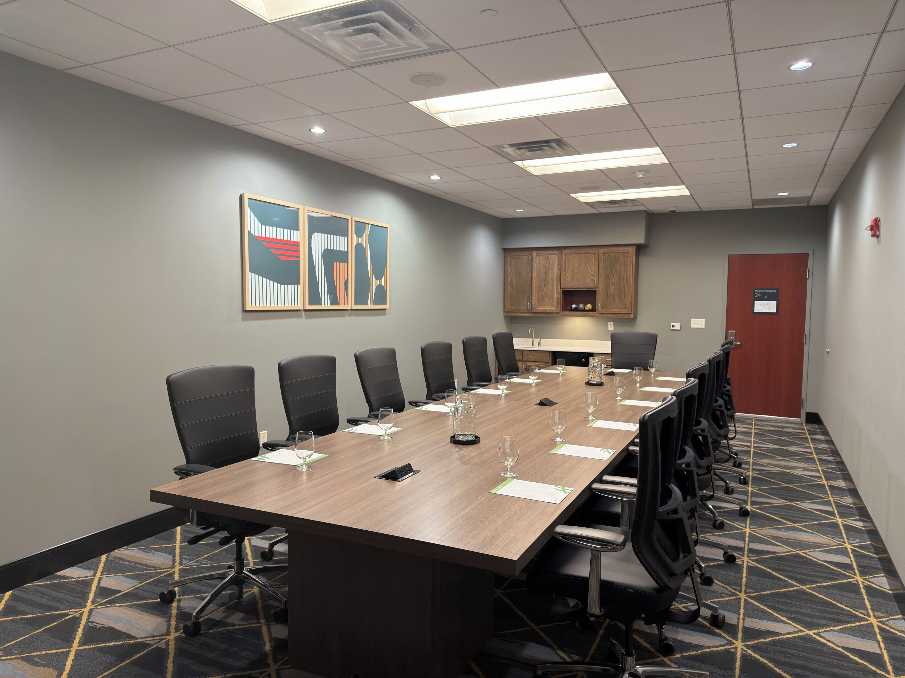 A conference room with a long table, chairs, a wooden cabinet, and a door.