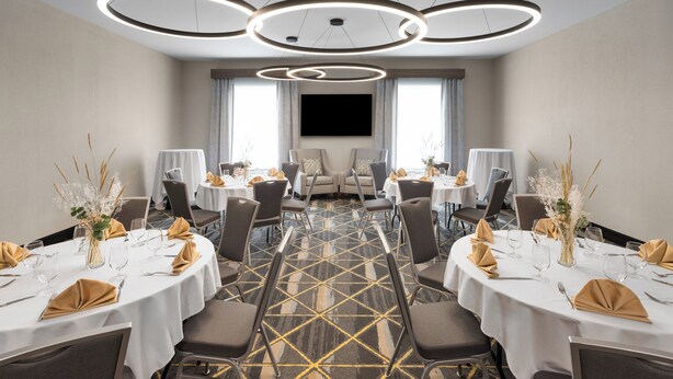 A conference room with round tables, chairs, a large TV screen, and a patterned carpet.