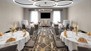 A conference room with round tables, chairs, a large TV screen, and a patterned carpet.
