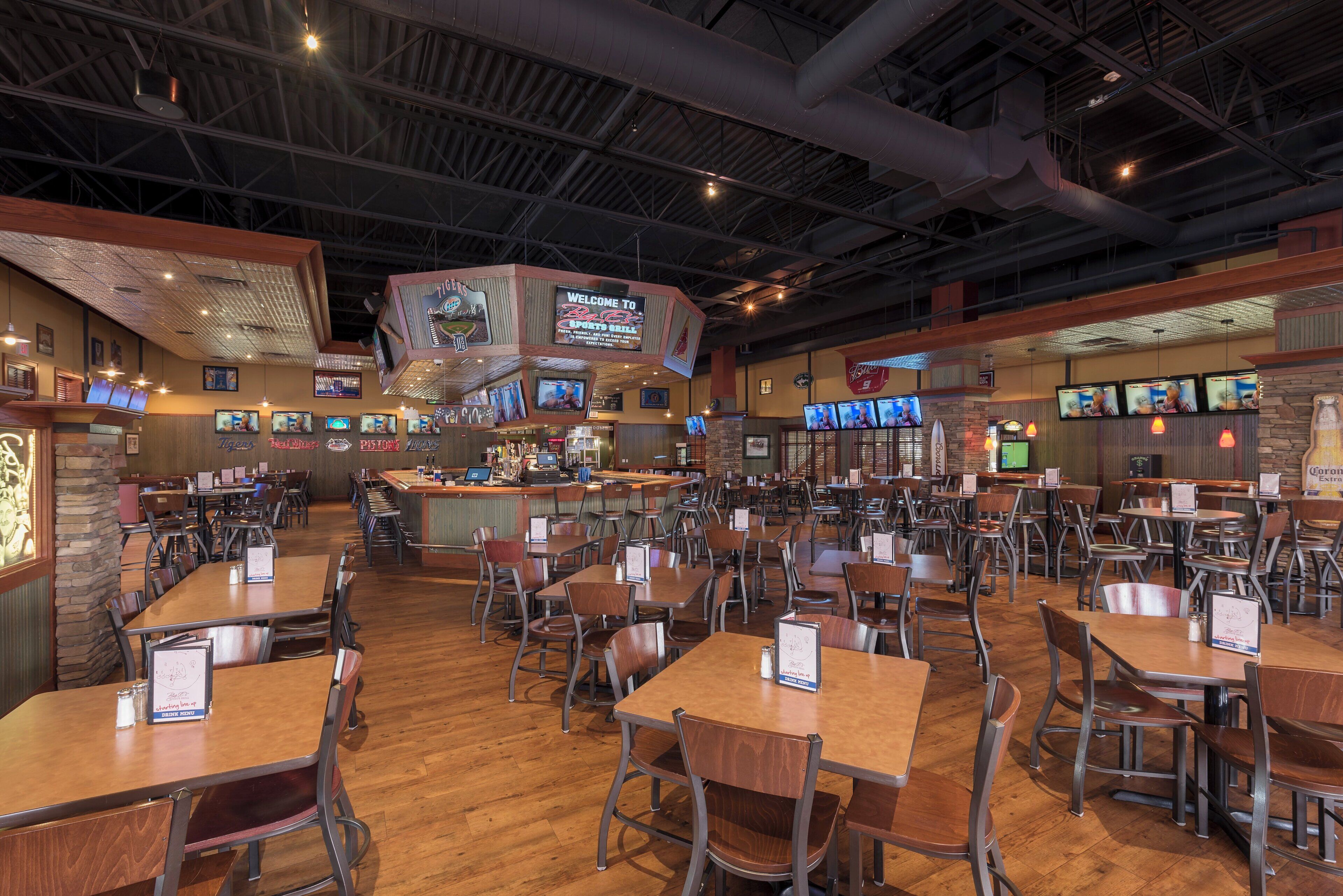 A spacious restaurant with multiple tables and chairs, a bar area, and several televisions mounted on the walls.