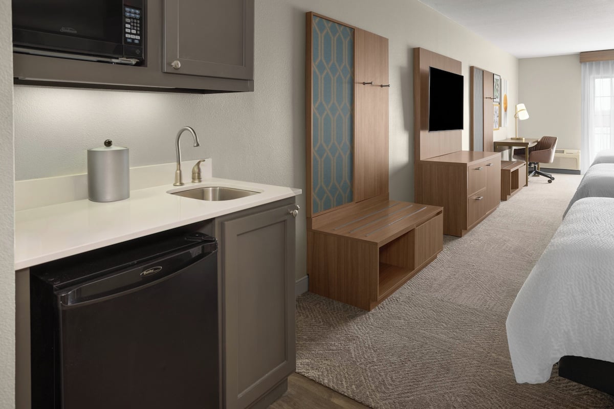 A hotel room with a kitchenette, a bed, a desk, and a TV.
