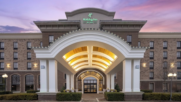 A Holiday Inn hotel entrance with a brick facade, arched entrance, and illuminated signage.