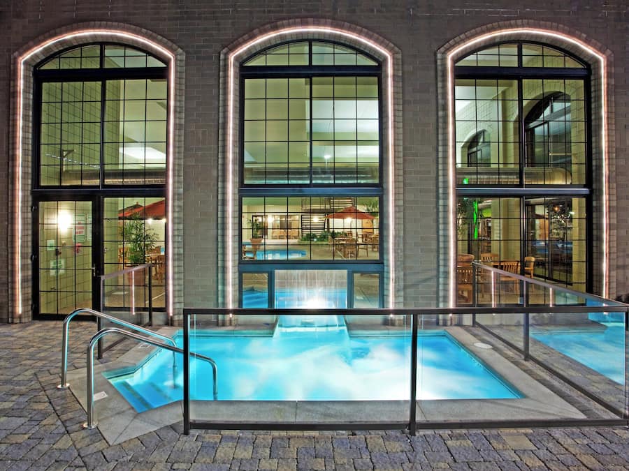 Um edifício com três grandes janelas em arco, área de piscina envidraçada e mobiliário de exterior visível pelas janelas.