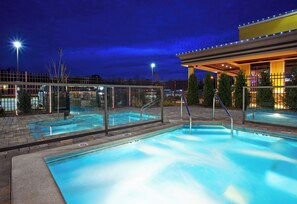 A swimming pool with a glass barrier, a covered area with lights, and a view of the surrounding area at night. - Holiday Inn Midland by IHG (Midland)