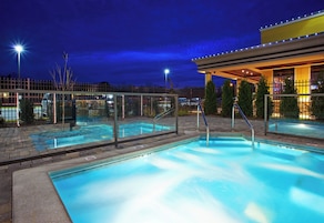 A swimming pool with a glass barrier, a covered area with lights, and a view of the surrounding area at night.