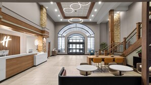 A spacious lobby with a reception desk, a staircase, and a seating area with tables and chairs.