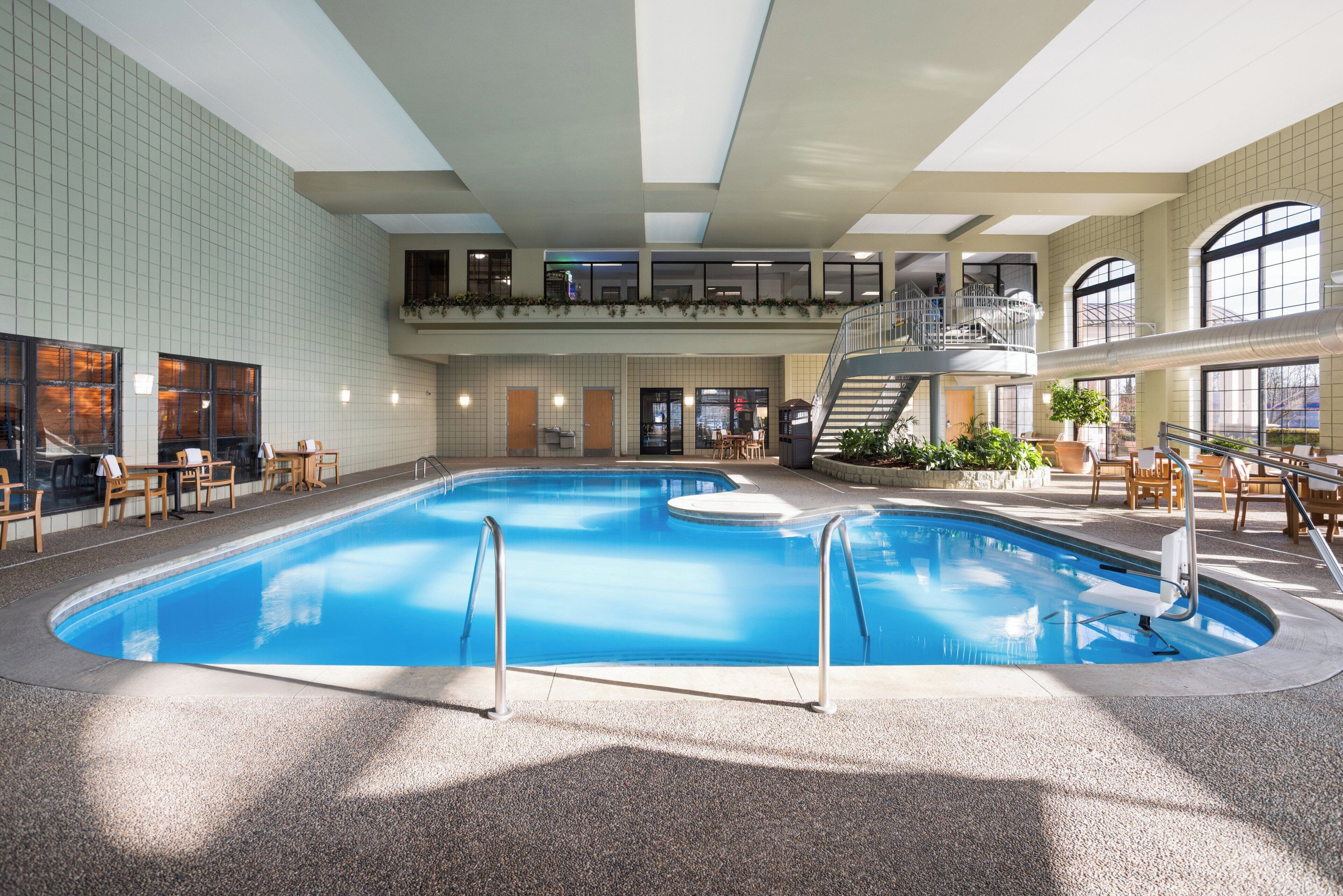Une piscine intérieure dotée d’une mezzanine, entourée d’espaces de détente et de plantes en pot.