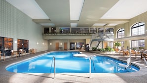 An indoor swimming pool with a mezzanine level, surrounded by seating areas and potted plants.