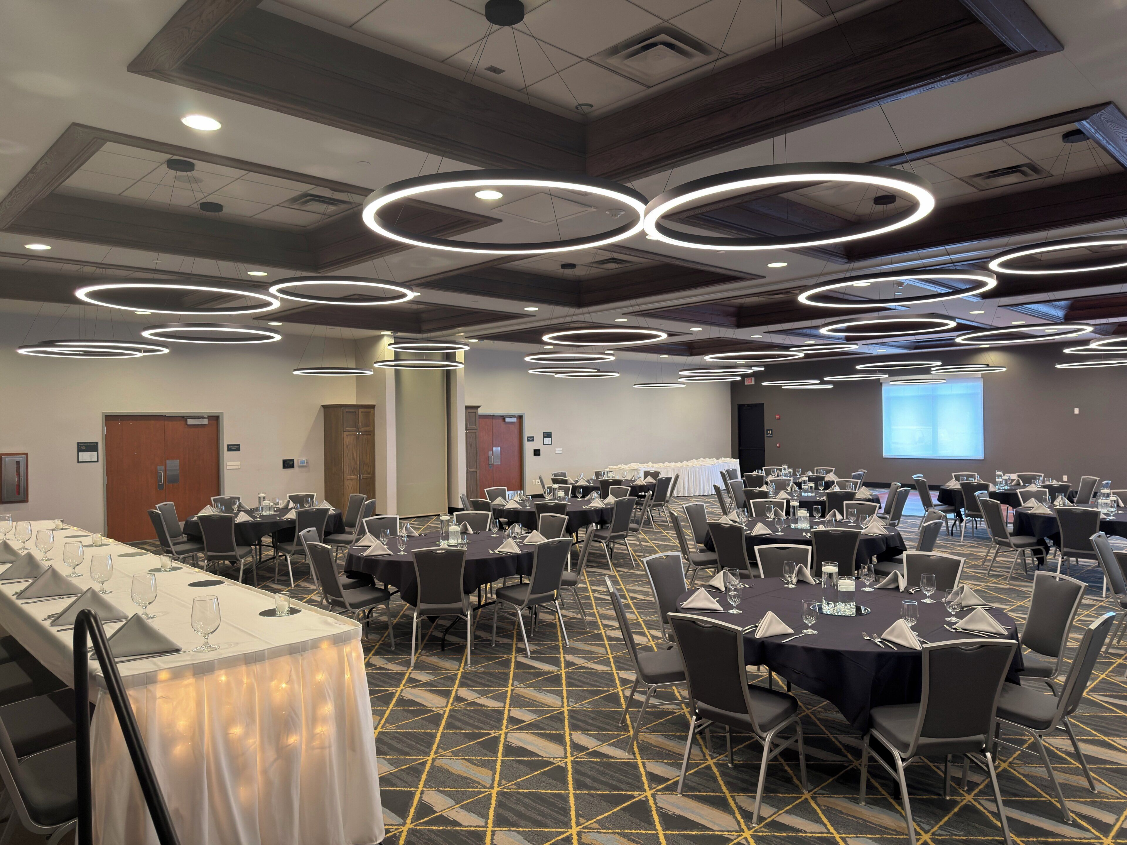 A conference room with round tables, chairs, and a projector screen.