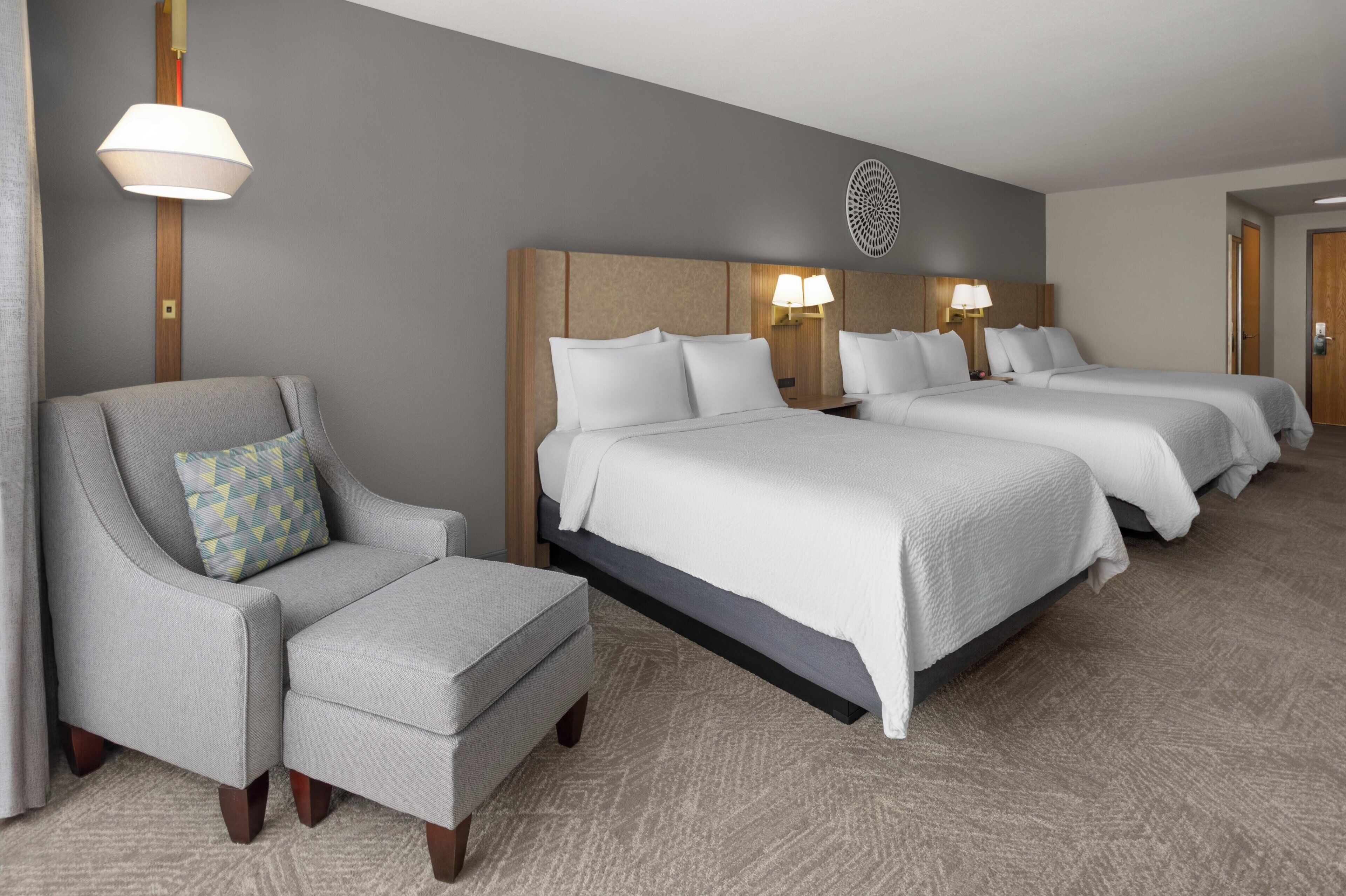 A hotel room with a sofa, two beds, a lamp, and a wall decoration.