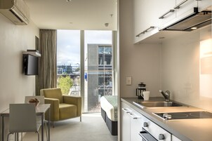 A modern hotel room with a balcony, a kitchenette, a dining area, and a bed.