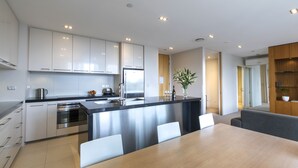A modern kitchen with stainless steel appliances, a central island with seating, and a dining area with a large table. - Quest Carlaw Park (Auckland)