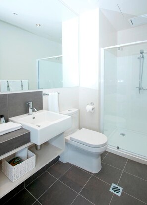 A modern bathroom with a large mirror, a sink, a toilet, and a glass-enclosed shower. - Quest Carlaw Park (Auckland)