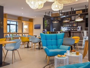 Ein modernes Interieur mit Barbereich, Sitzgelegenheiten mit bunten Stühlen und einem großen blauen Sofa.