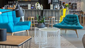 A modern bar area with blue sofas, a white coffee table, and a bar counter with bottles and glasses. - Hôtel ibis Lyon Sud Vienne Saint Louis (Vienne)