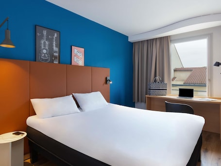 A hotel room with a bed, a desk, a laptop, and a window with curtains.