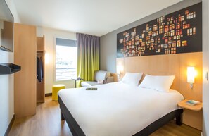 Une chambre d’hôtel avec un grand lit, une chaise, une petite table et une fenêtre avec des rideaux.