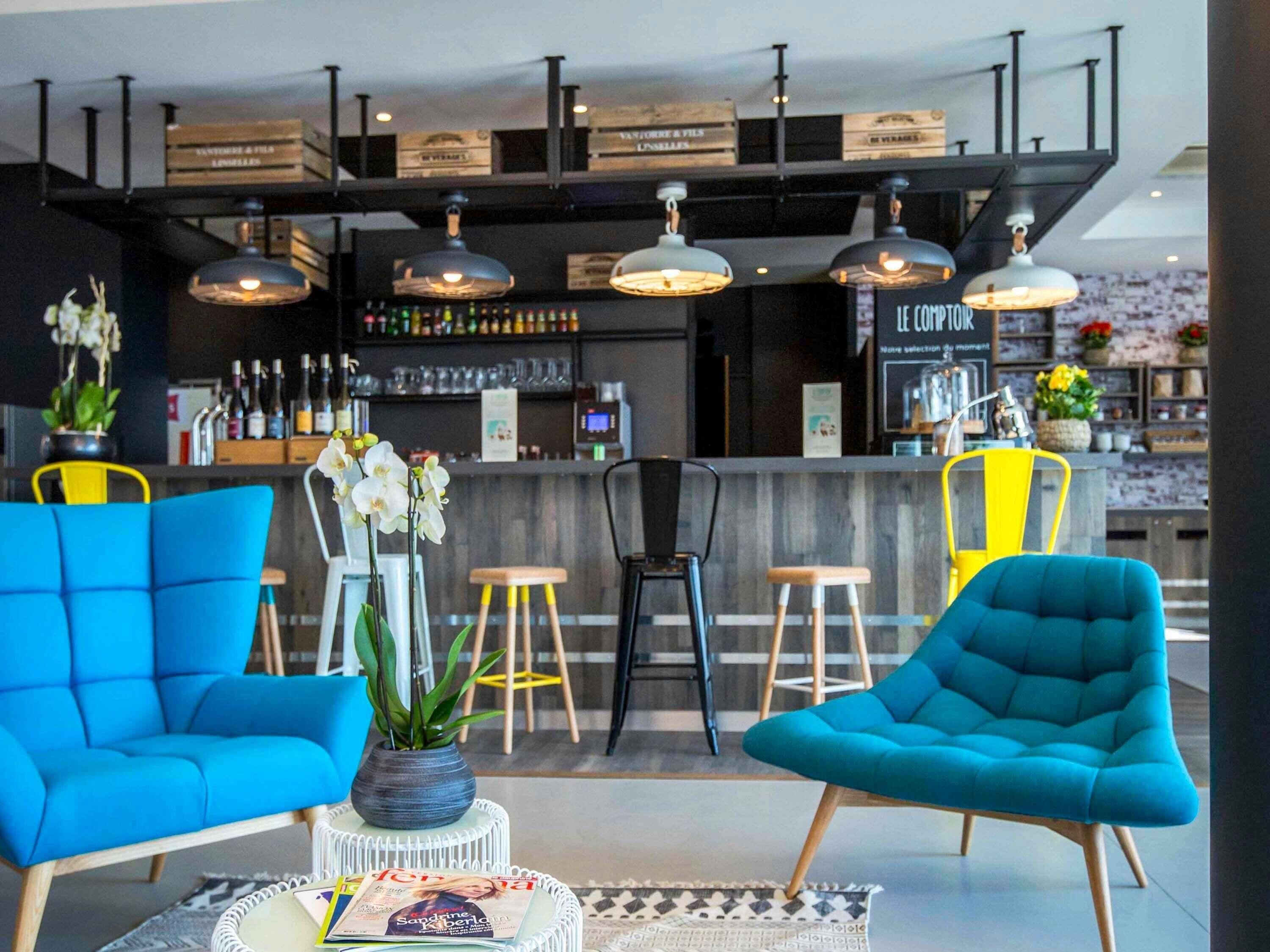 A modern bar area with blue chairs, a bar counter, and overhead lighting.