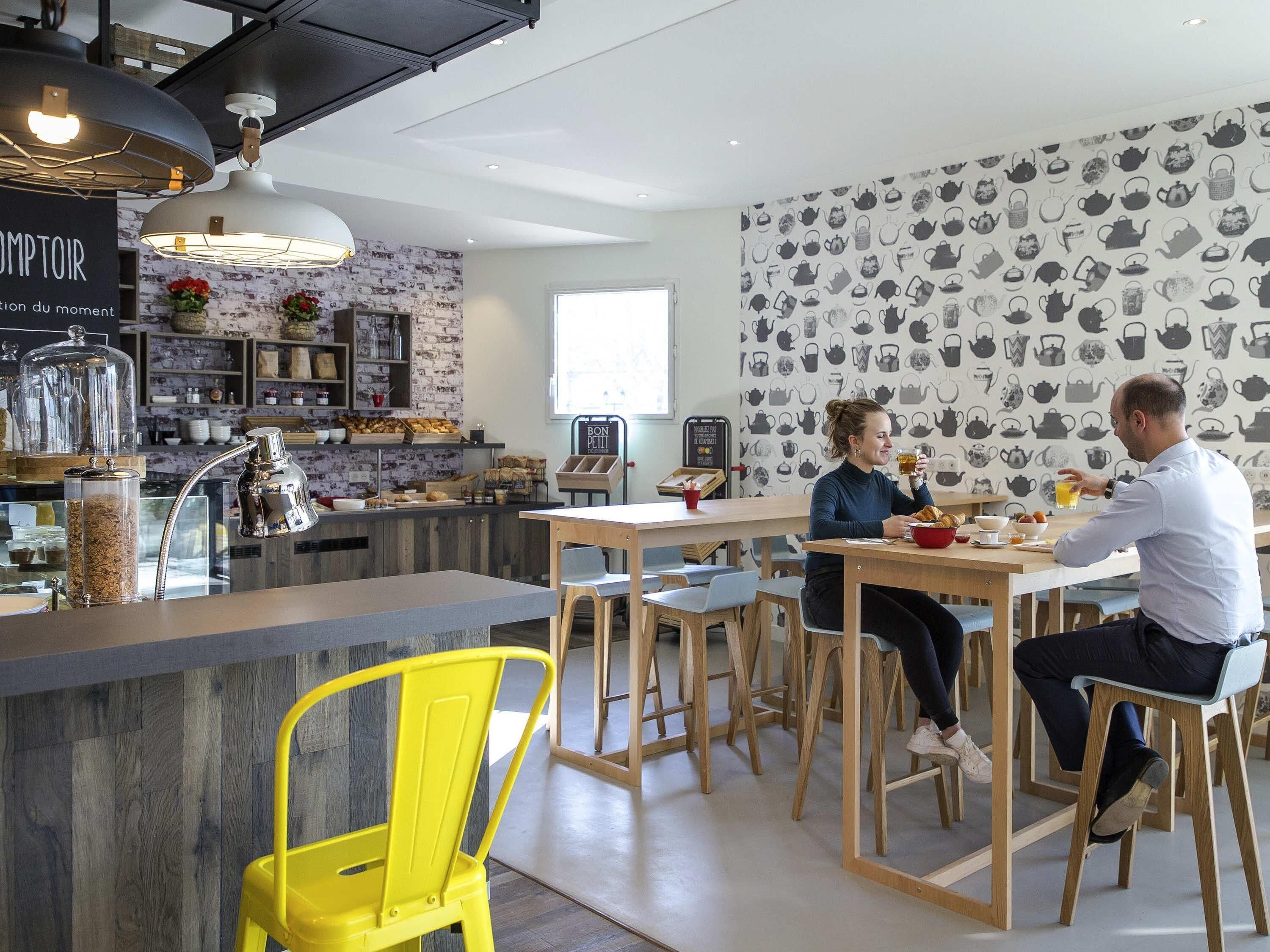 A modern café with a bar area, seating, and a wall with a tea kettle pattern.