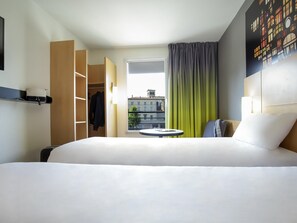Ein Hotelzimmer mit Bett, einem kleinen runden Tisch, einem Kleiderschrank und einem Fenster mit Vorhängen.