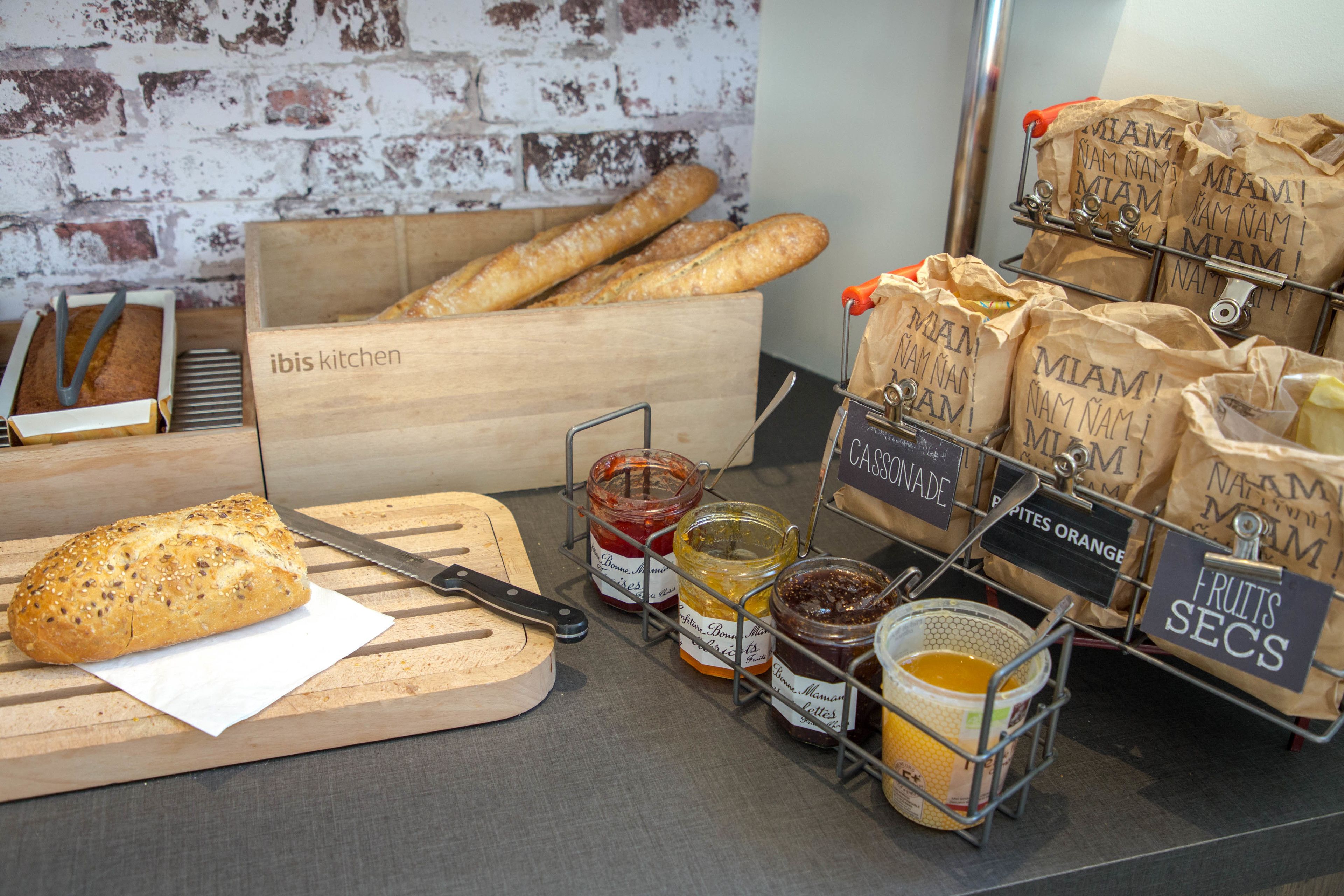 A kitchen counter with bread, jars of preserves, and a cutting board.
