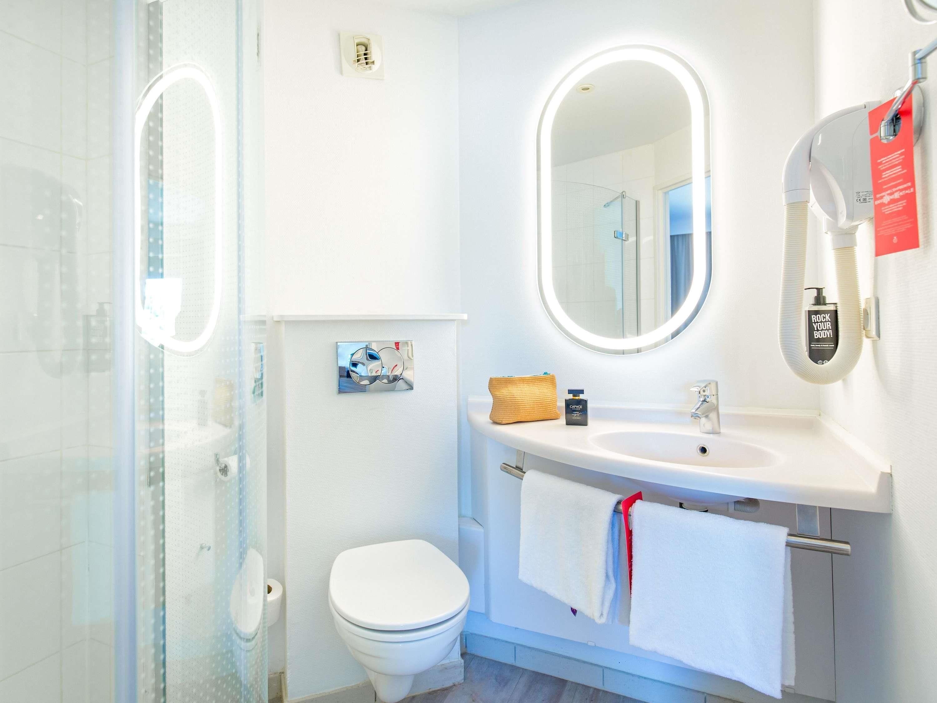 Un baño moderno con cabina de ducha de vidrio, inodoro blanco, tocador con espejo y toallero.