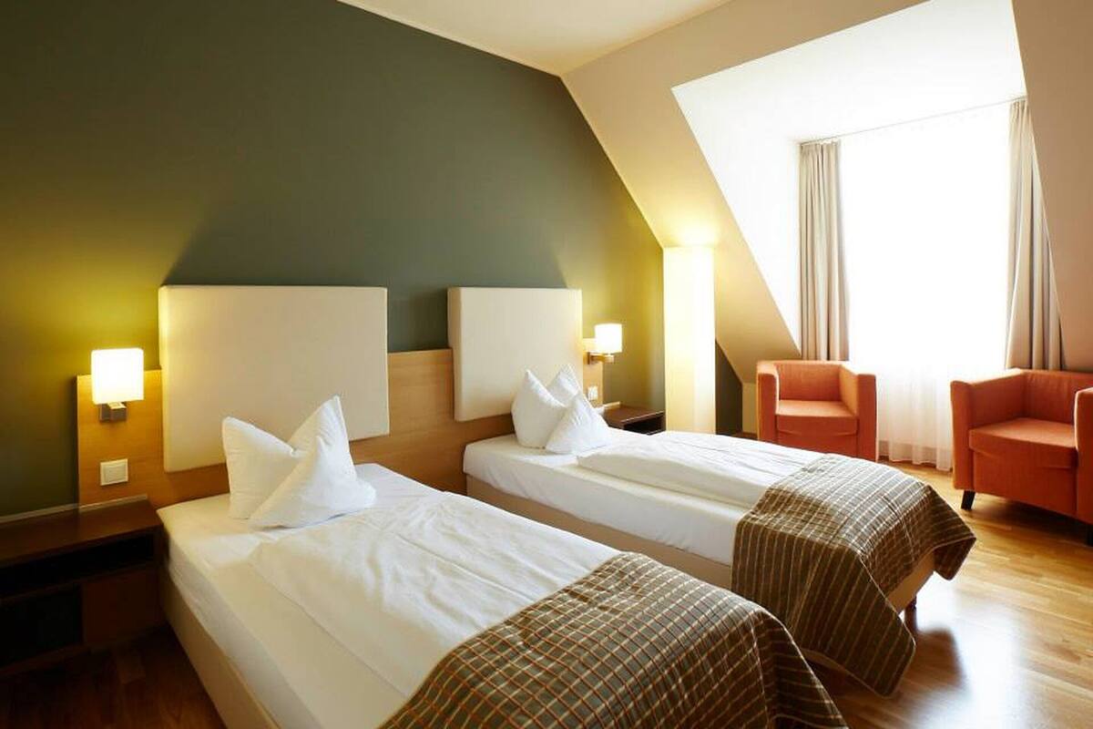 A hotel room with two beds, a sofa, a lamp, and a window with curtains.