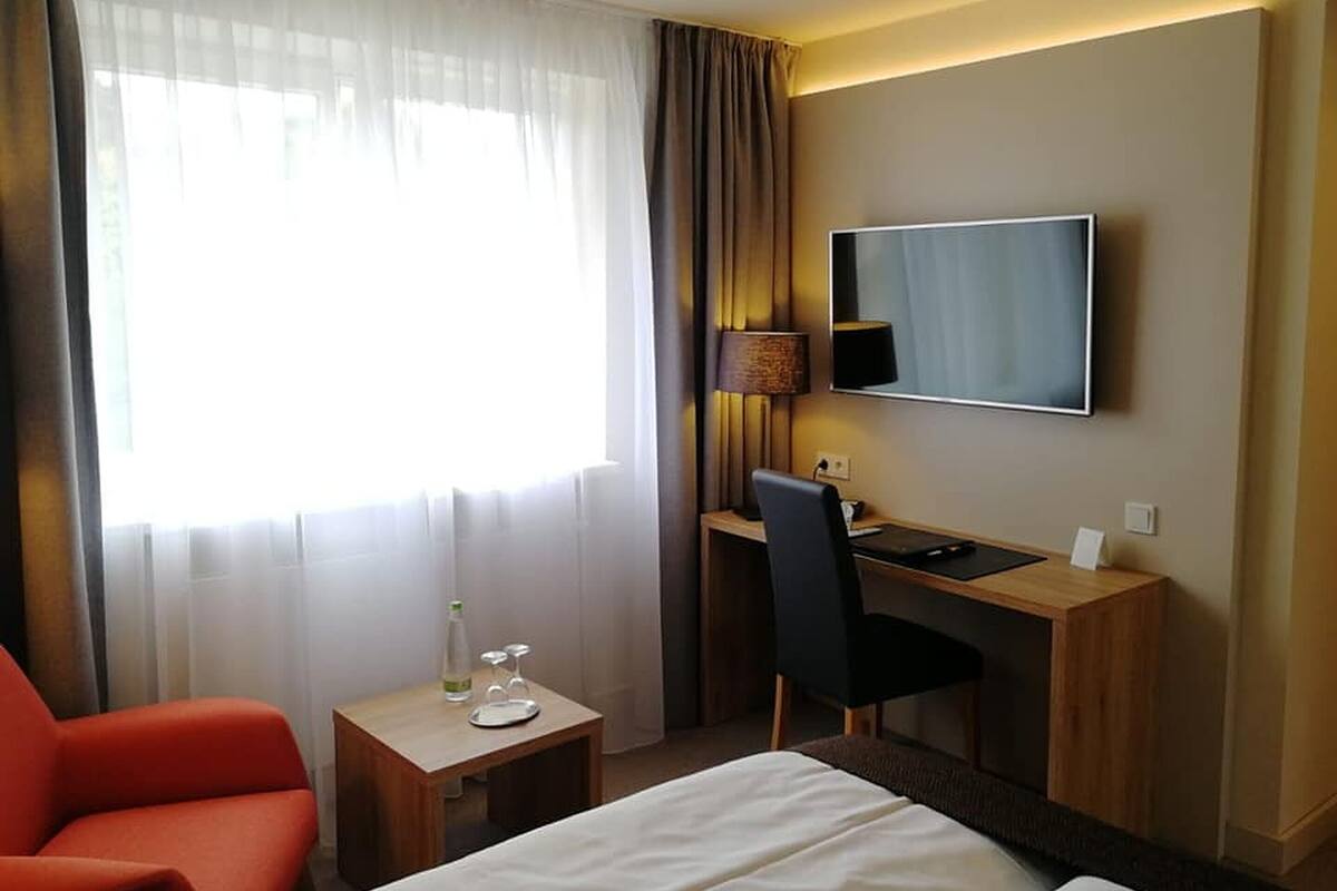 A hotel room with a bed, a desk, a chair, a TV, and a window with curtains.