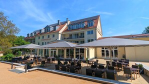 Een hotel met terras, meerdere eetgelegenheden en een groot gebouw met een pannendak.