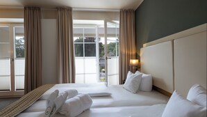 Een hotelkamer met twee bedden, een groot raam met gordijnen en uitzicht op buiten.