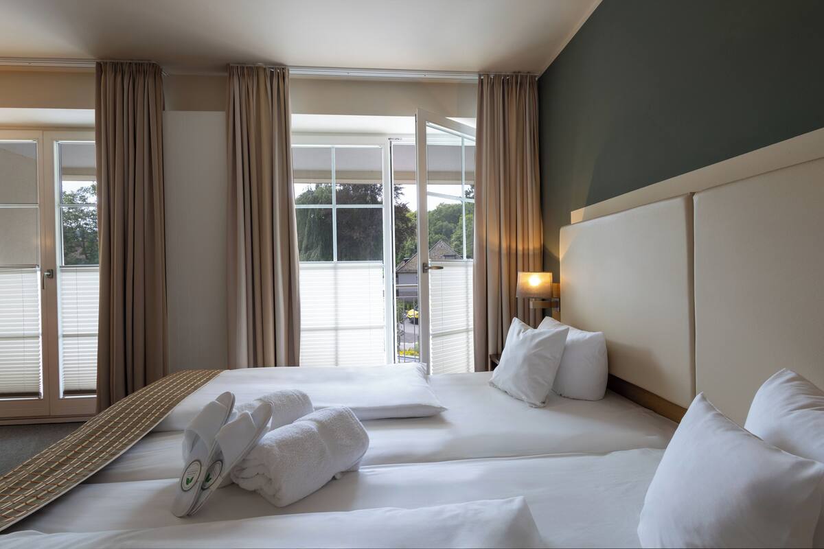 A hotel room with two beds, a large window with curtains, and a view of the outside.
