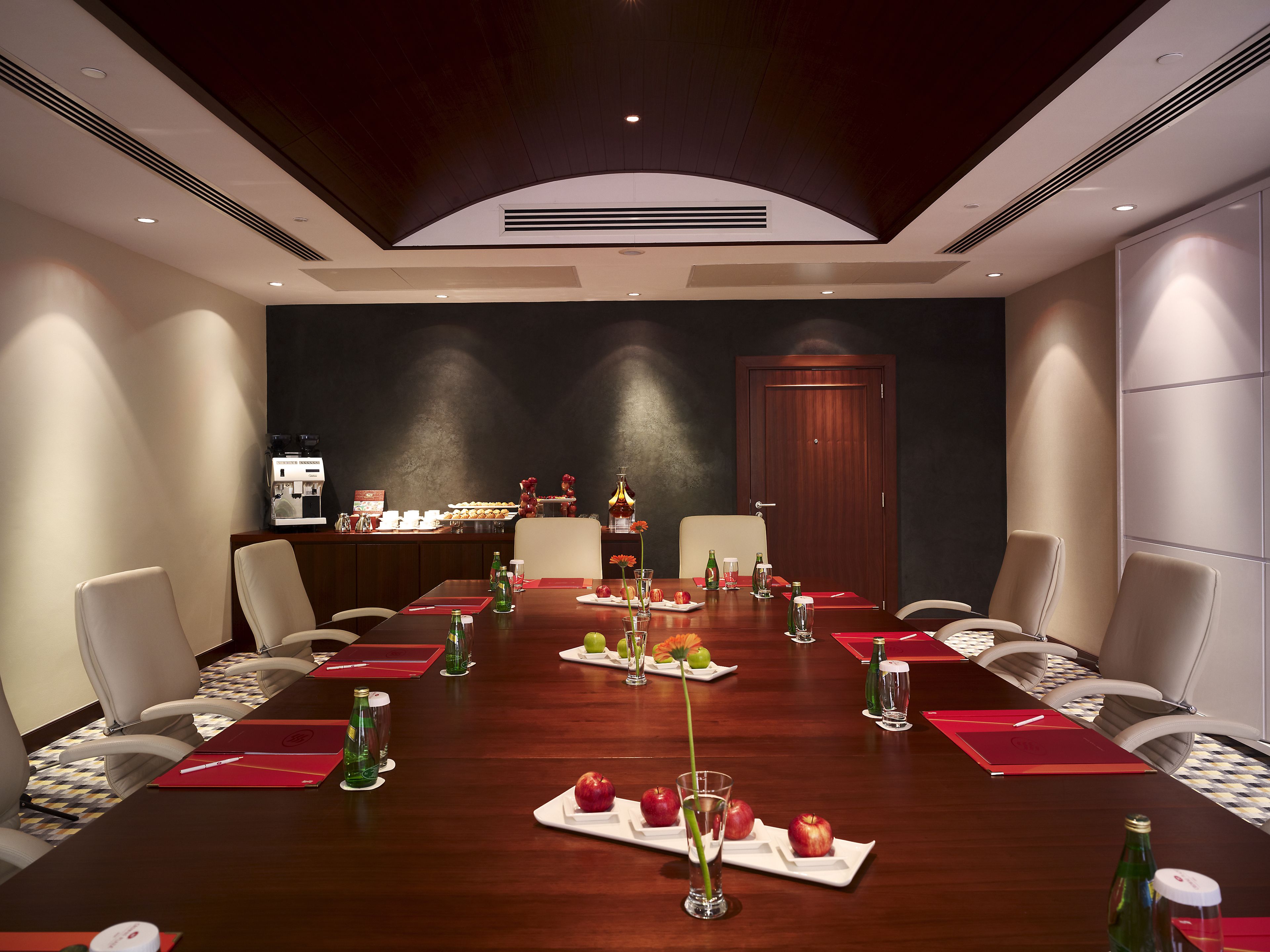 A conference room with a long table, chairs, and a buffet area in the background.