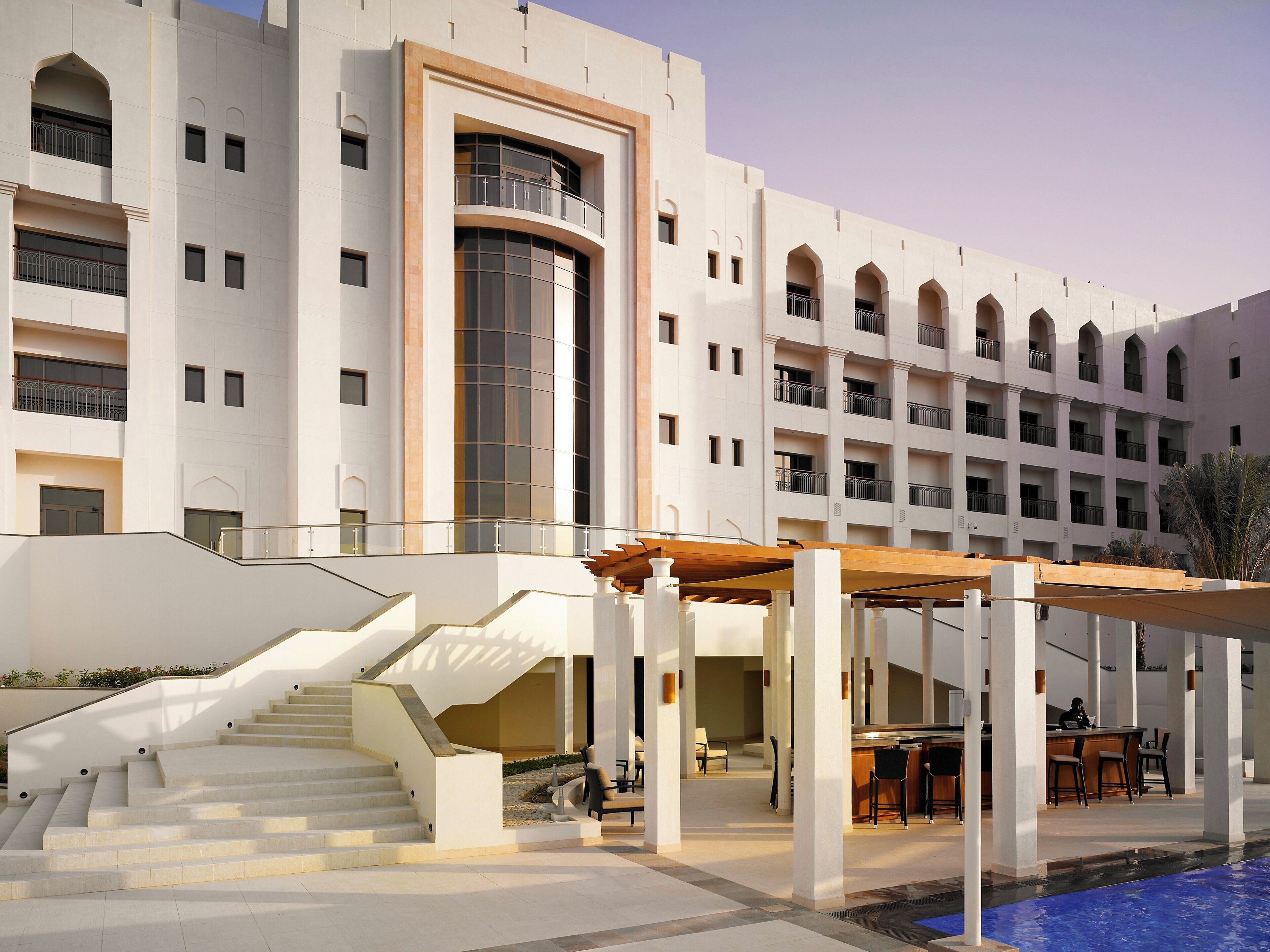 A multi-story hotel with a pool area, outdoor seating, and a staircase leading to the upper floors.
