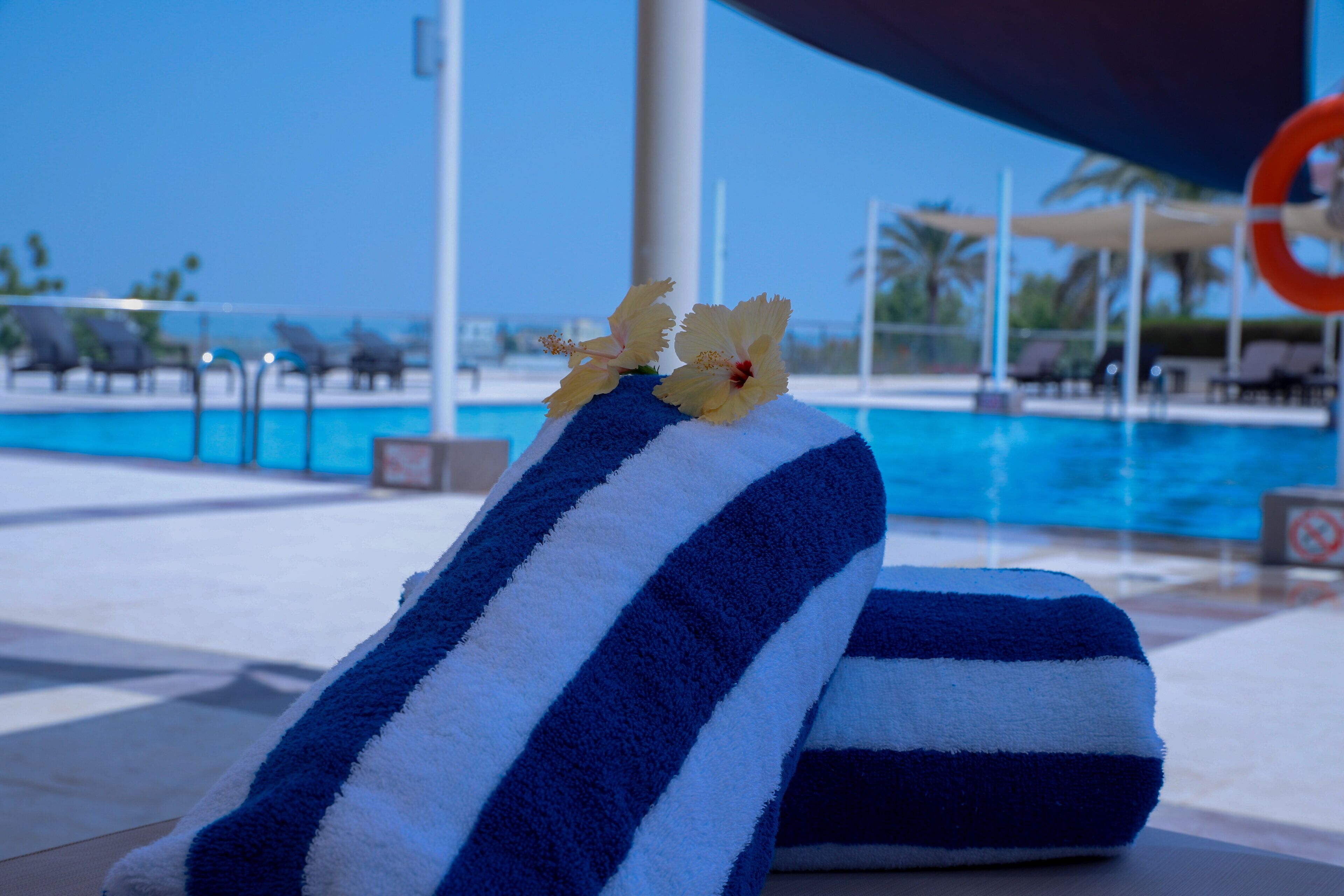 A towel with a blue and white striped pattern and a yellow flower on a poolside area.